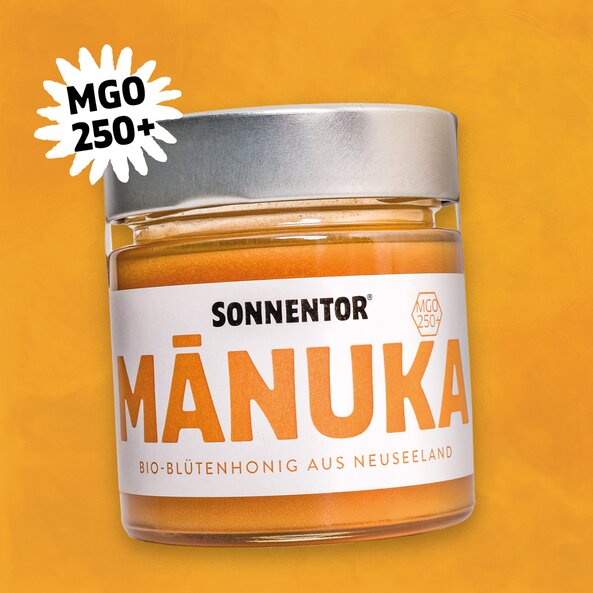SONNENTOR MÁNUKA organic blossom honey from New Zealand in a jar with a silver lid and the icon ‘MGO 250+’ on an orange background.