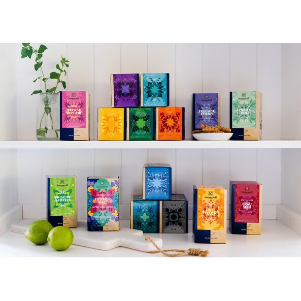 Auf dem Bild sind alle Tee Packungen der Reihe Happiness Is zu sehen. Sie stehen in einem Regal auf zwei Etagen verteilt.