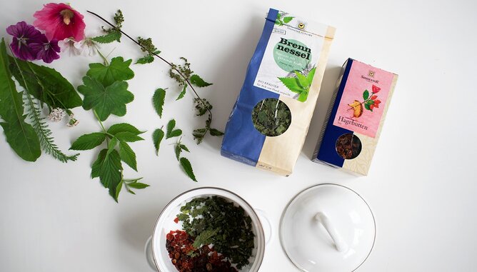 Reichl Karina Teezubereitung | © SONNENTOR Foto von einer Packung Hagebuttentee und Brennnesseltee. Daneben sieht man die Teemischung in einem Topf. | © SONNENTOR